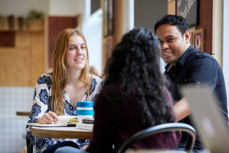 Three students sitting at a table together chatting and smiling.